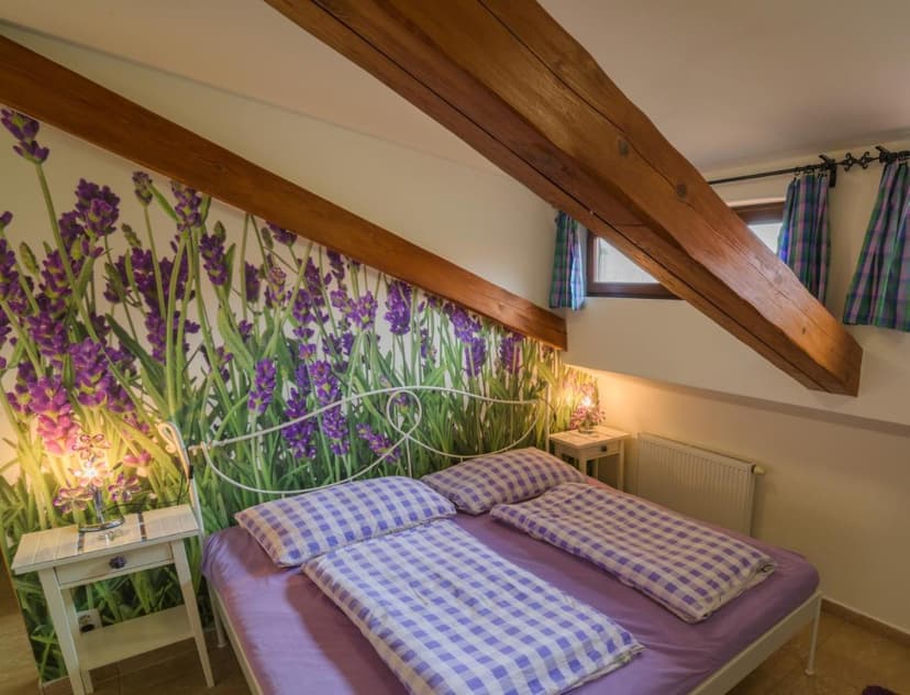 Bedroom with lavender mural, wood beams, and white metal bed with gingham bedding in Melnik room.