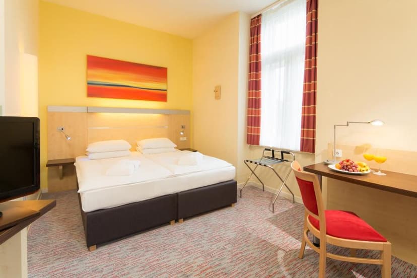 Hotel room with twin beds, yellow walls, and a desk with fruit and juice in Prague.
