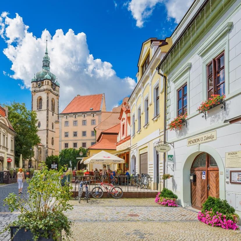 Cobblestone square with historic buildings, outdoor cafe, and church tower in Melnik, Czechia.