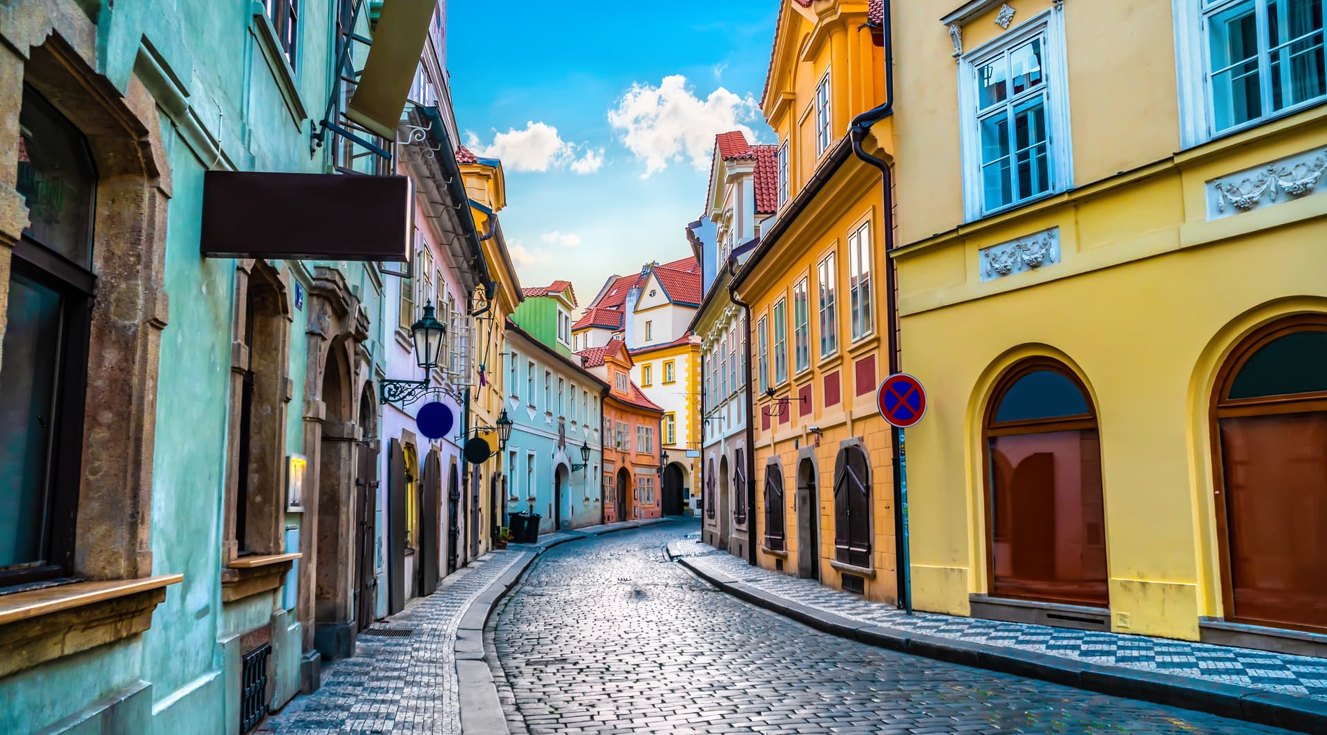 Cobblestone street winding between colorful historic buildings under a bright blue sky in Prague.