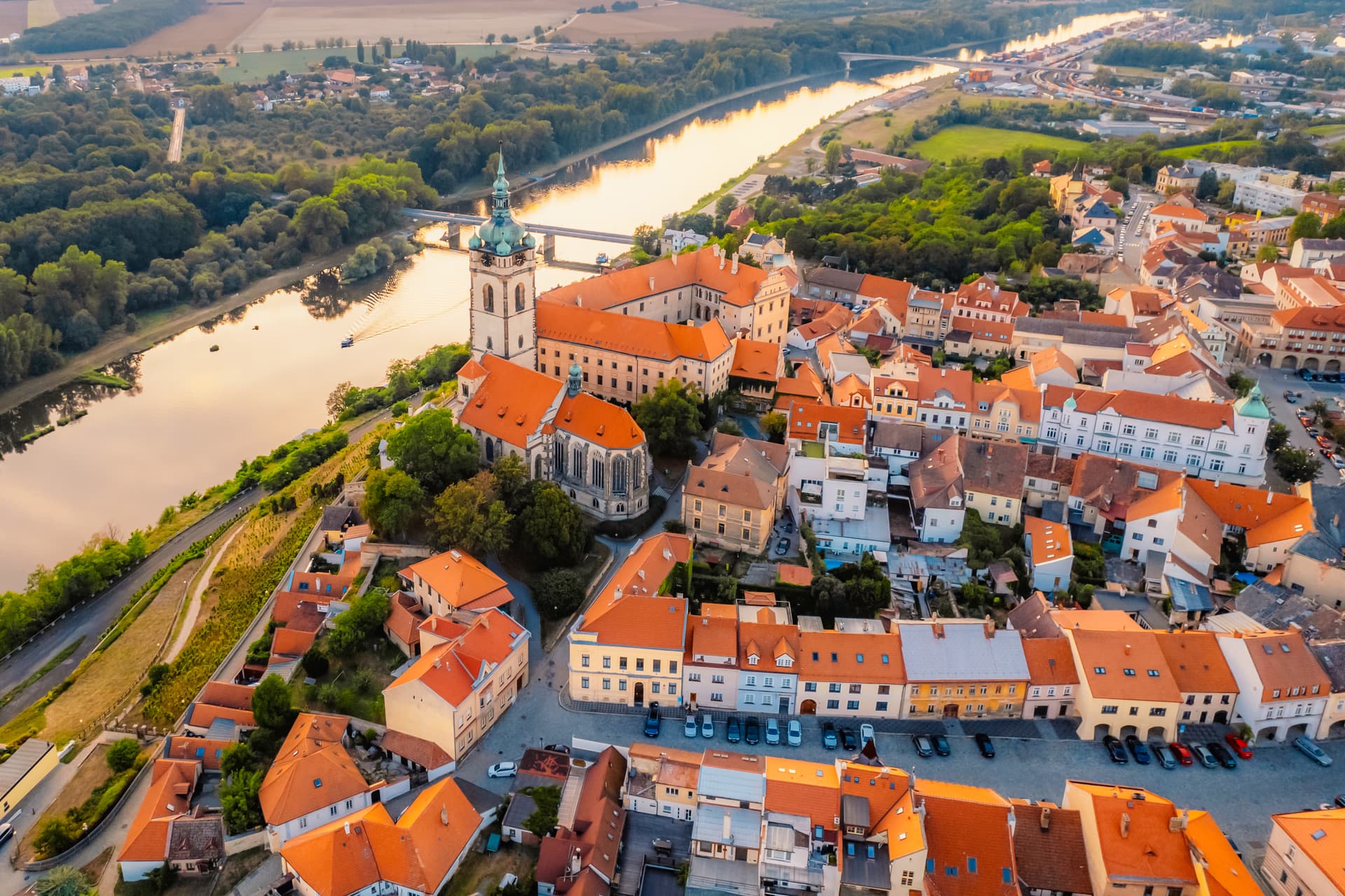 Aerial view of Melnik town with orange roofs, church tower, and river reflecting sunset light.