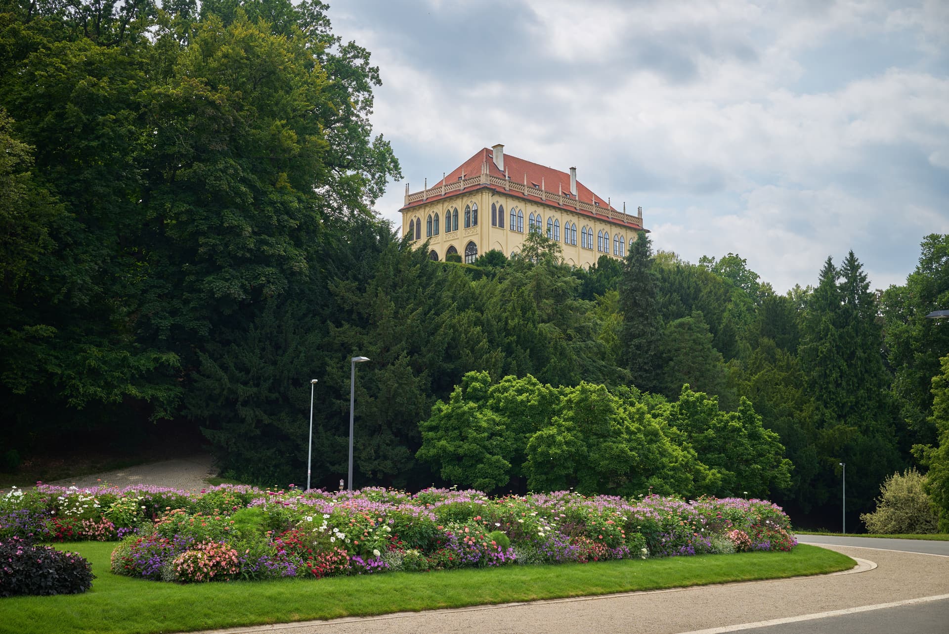 Yellow building with a red roof on a hill surrounded by dark green trees in Prague park.