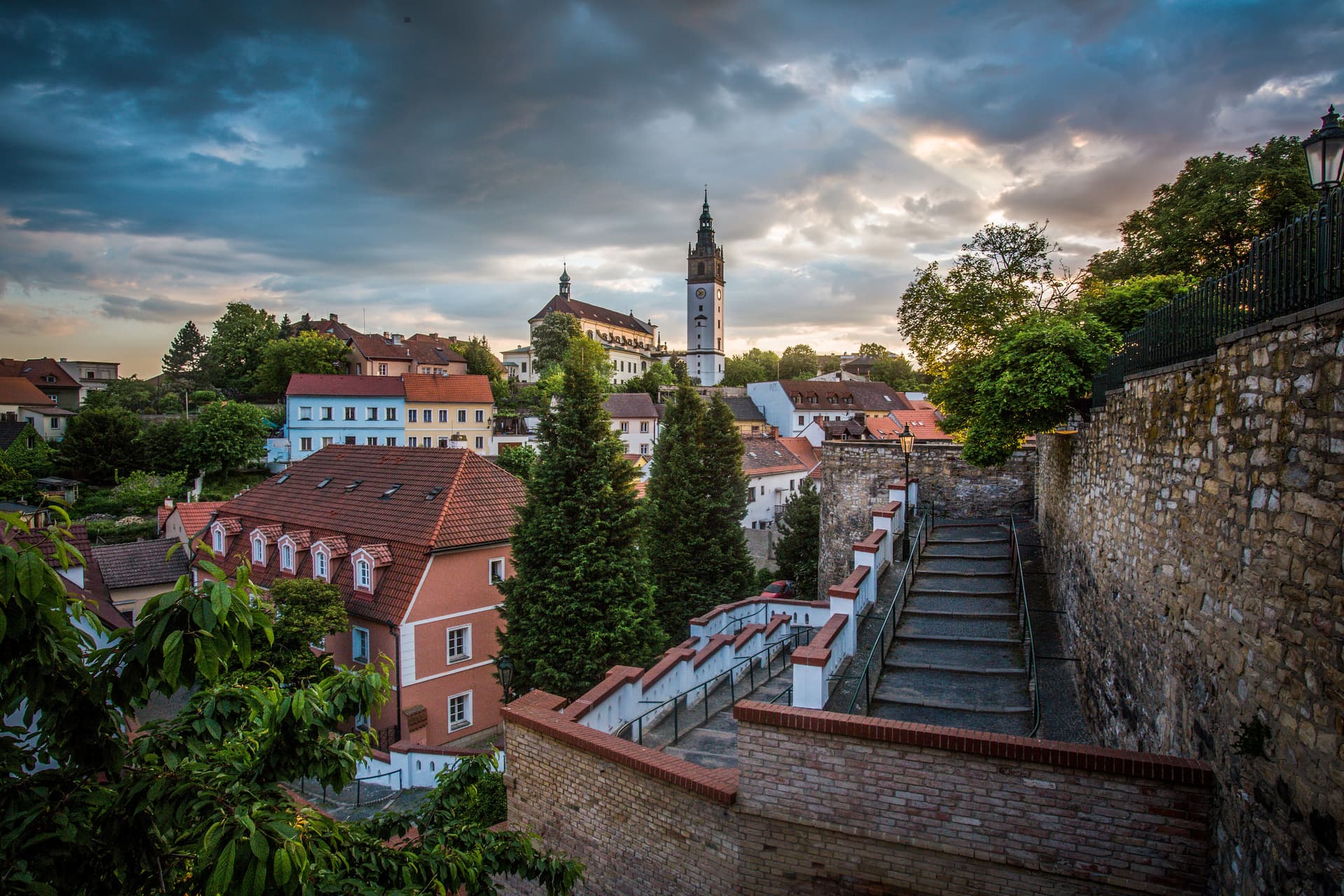 Historic town of Litomerice with colorful houses and a prominent white tower under dramatic sunset clouds.