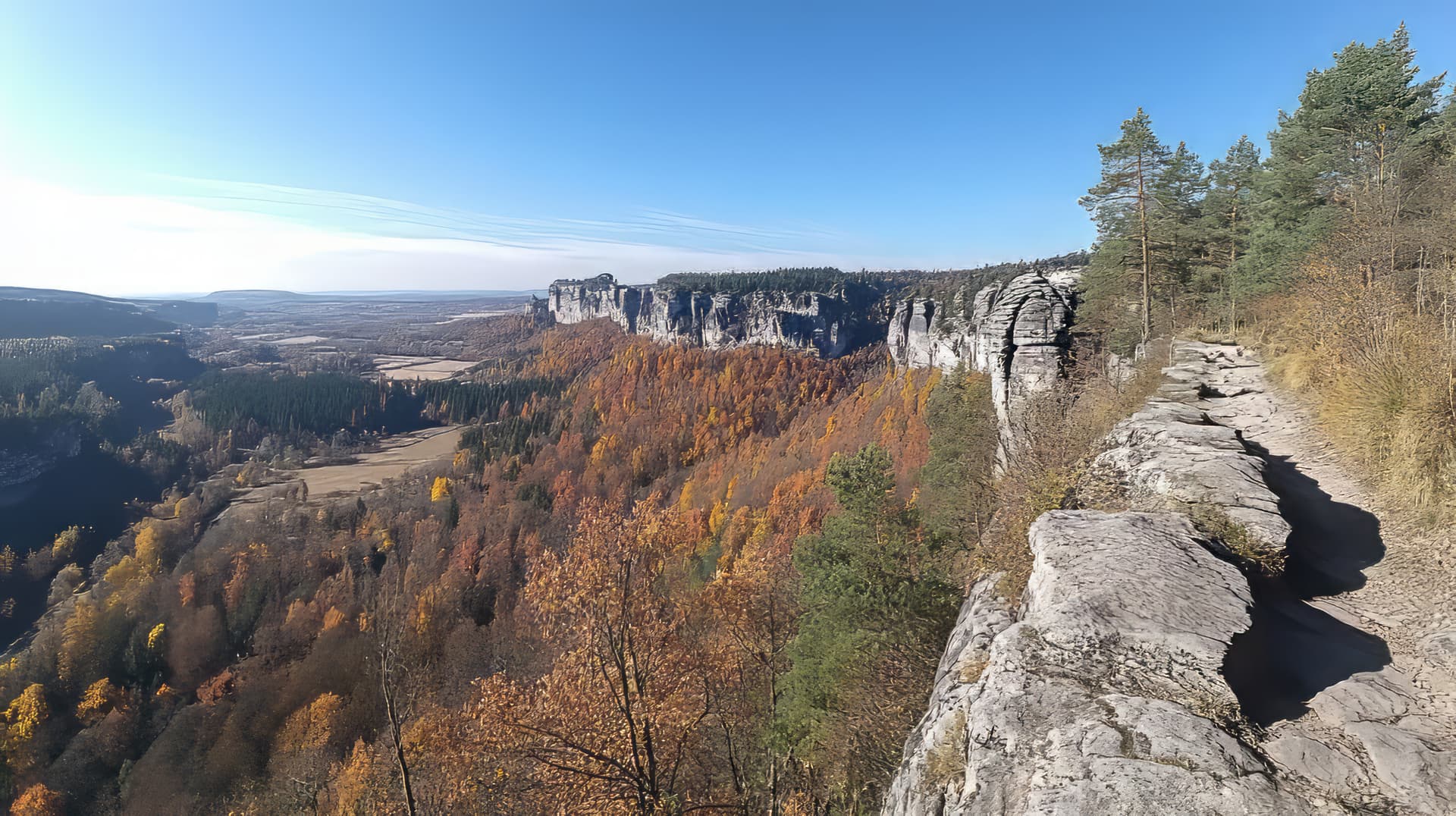 Hiking trail on rocky outcrop overlooking Bohemian Switzerland cliffs and autumn forest