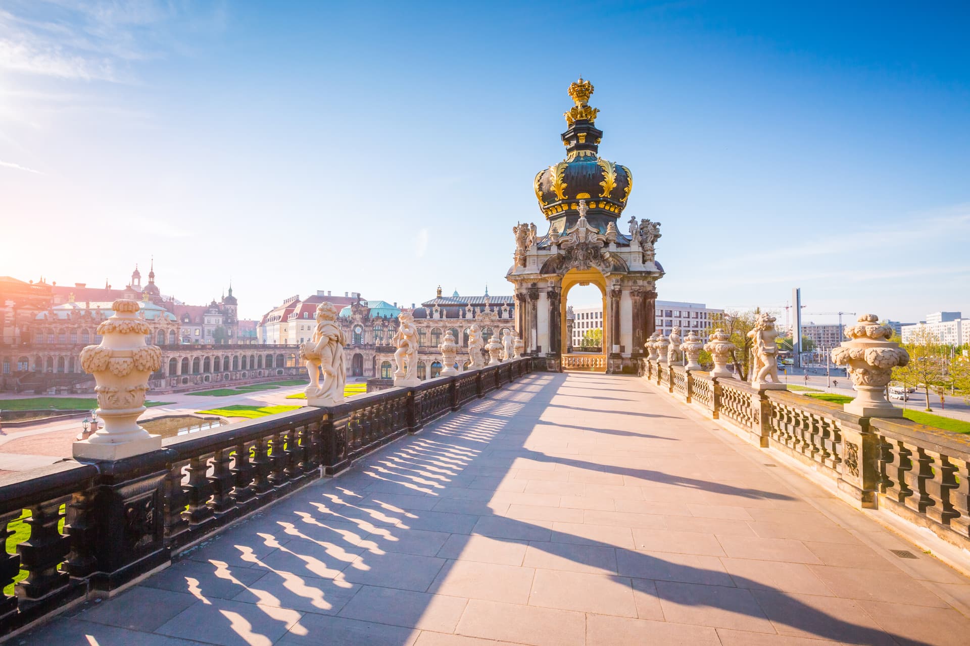Baroque balcony with statues and golden crown ornament overlooking Dresden Zwinger courtyard.