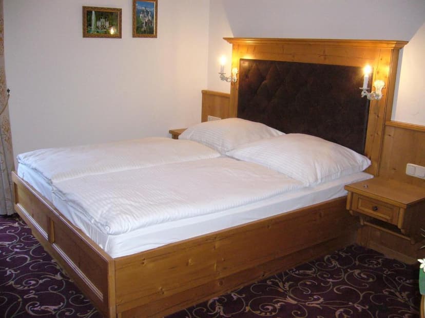 Wooden bed with white linens, dark patterned carpet, and two wall sconces in Schongau room.