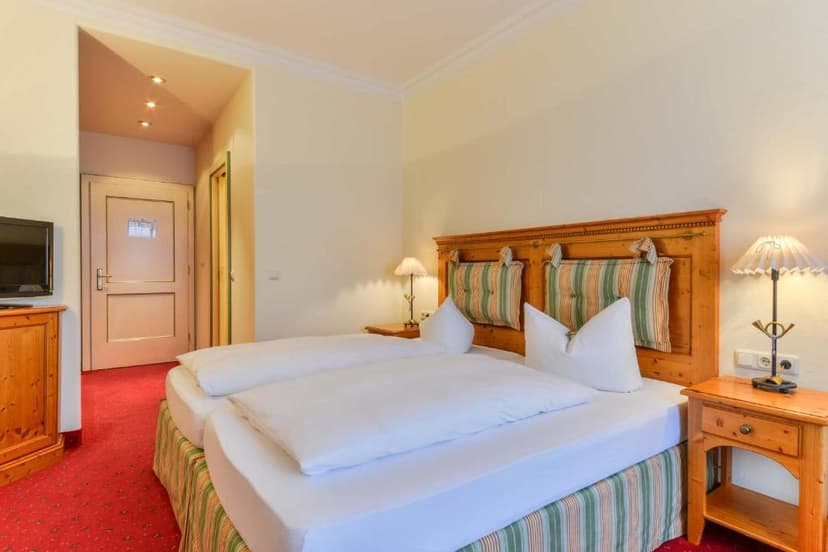 Twin beds with white duvets in a hotel room with wood furniture and red carpet, Murnau.
