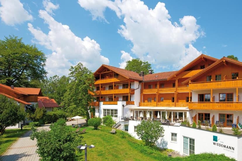 Hotel Wiedemann with wooden balconies and green lawn under a blue sky with clouds