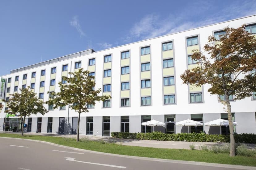 Holiday Inn Express hotel exterior with white facade, trees, and outdoor umbrellas in Augsburg.