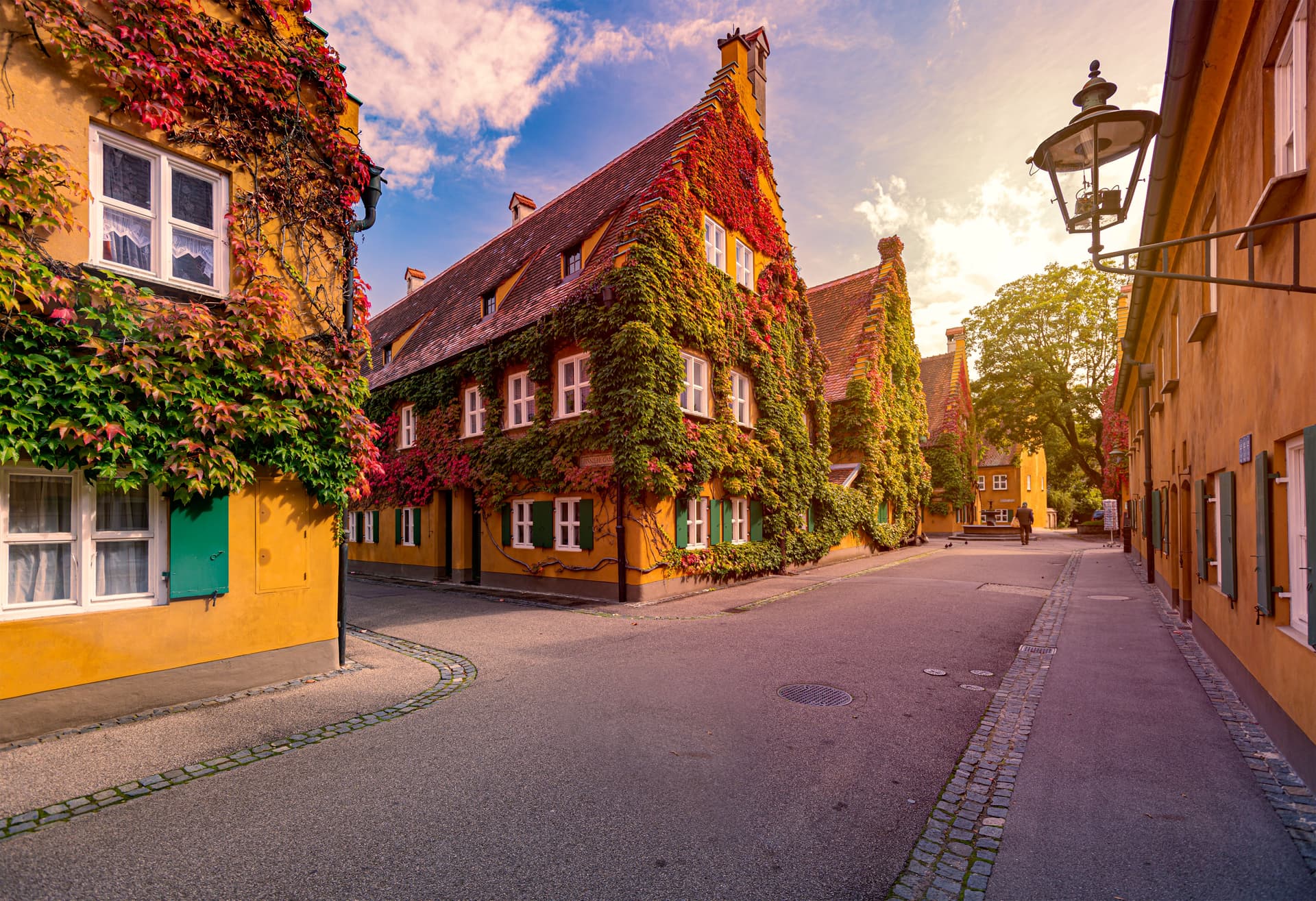 Fuggerei buildings covered in autumn ivy on a quiet street with cobblestone accents.