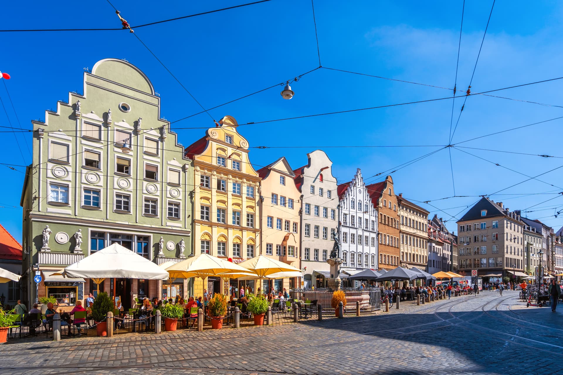 Outdoor cafe dining on cobblestone main square with colorful historic buildings and clear blue sky.
