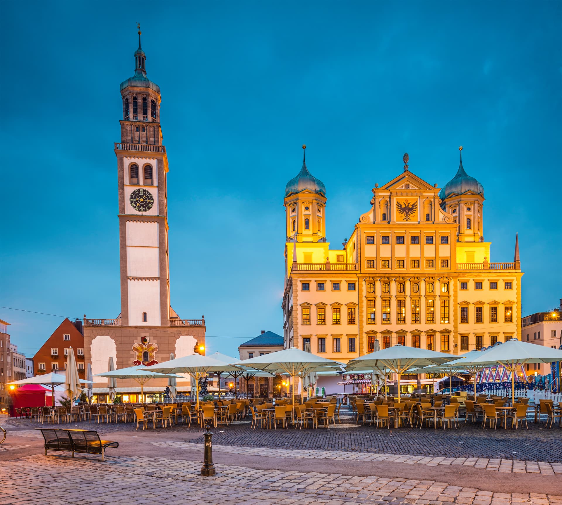 Historic town square with illuminated Rathaus and empty outdoor cafe seating at twilight