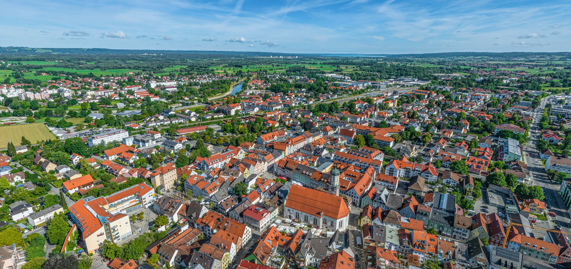 Aerial view of Weilheim town center with red-tiled roofs, green landscape, and a river under a blue sky.