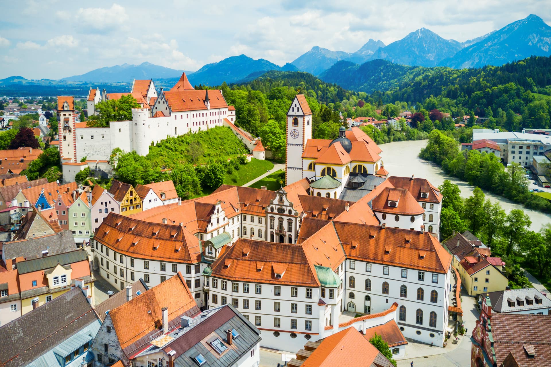 Historic town of Füssen with white buildings, orange roofs, and green mountains in the background.
