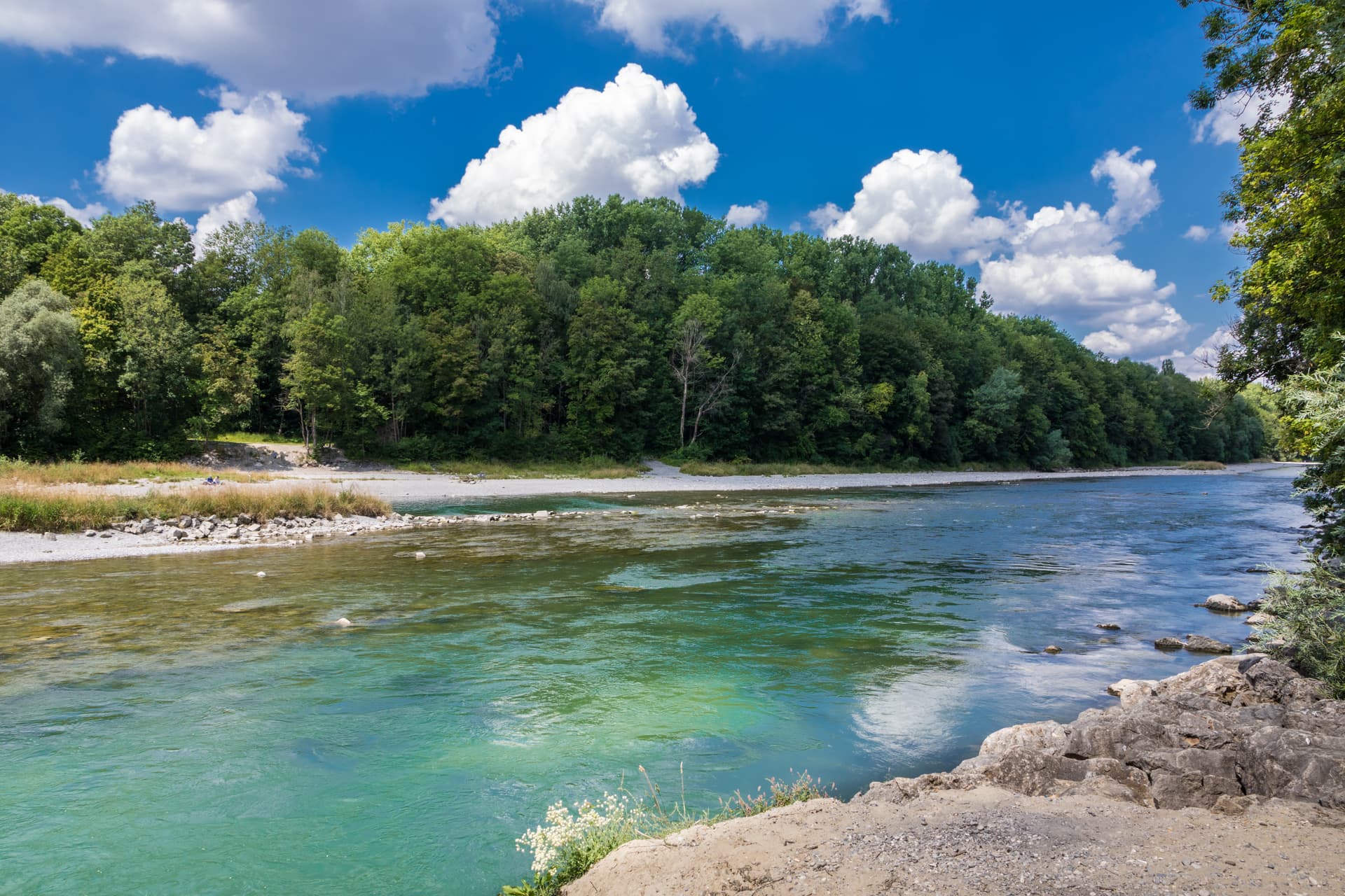 Turquoise Lech River flowing past a gravel bank and dense green forest under a blue sky.