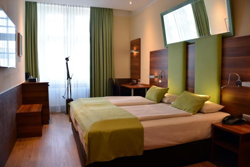 Twin hotel room with wood paneling, green accents, and bright window with sheer curtains.