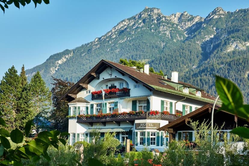 Hotel Astoria in Garmisch with balconies and green shutters against a forested mountain backdrop.