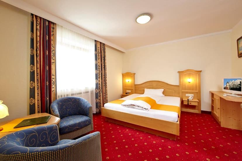 Hotel room with wooden bed, blue armchairs, and bright red patterned carpet in Wallgau.