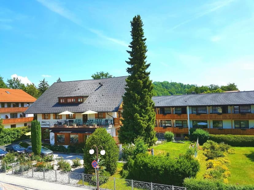 Hotel building with dark roof, green lawn, and tall evergreen tree under blue sky in Bad Tölz.