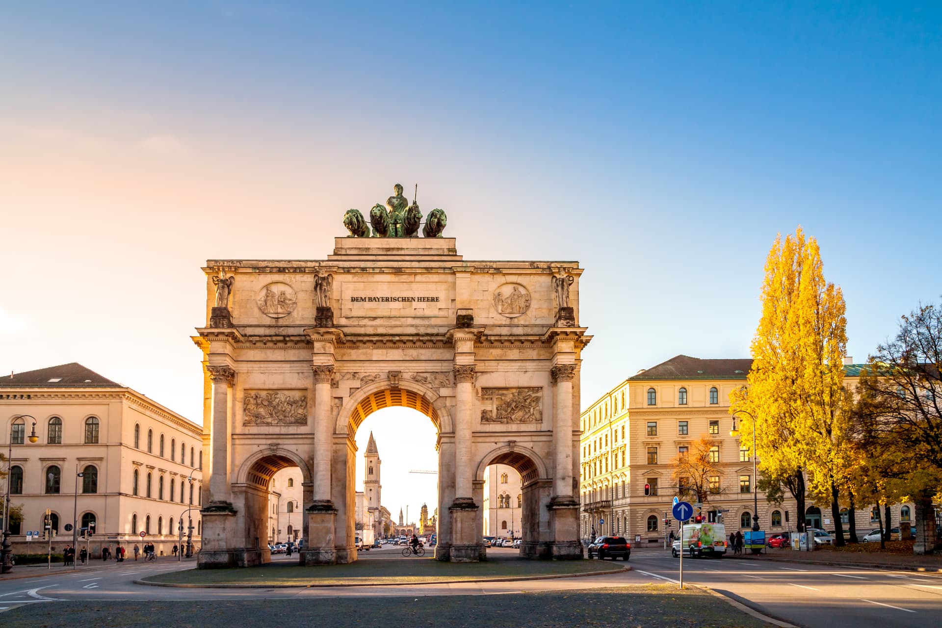 Munich Victory Gate (Siegestor) with autumn foliage and clear blue sky.