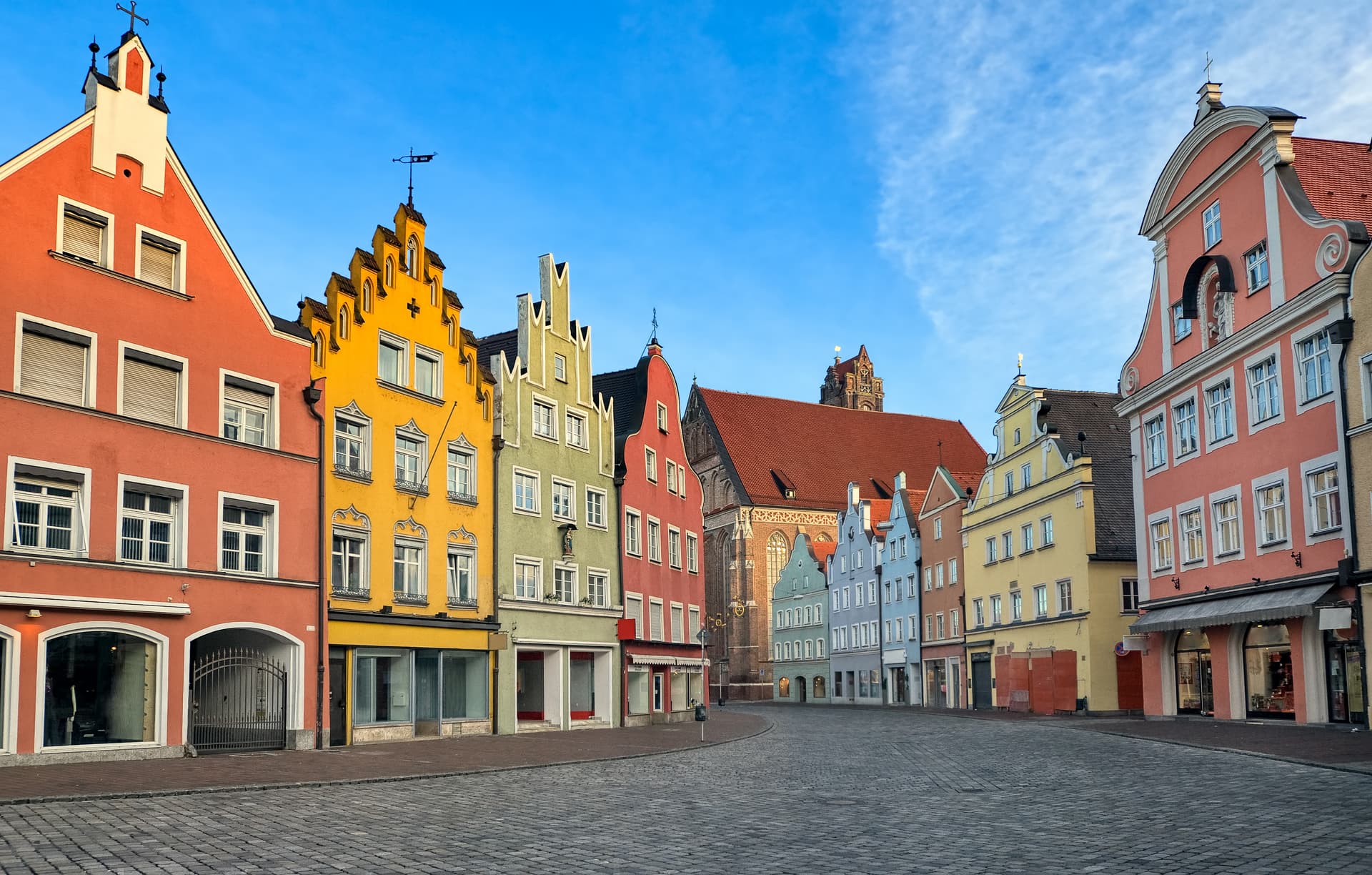 Colorful historic buildings line a cobblestone square in Munich's old town under a bright blue sky.