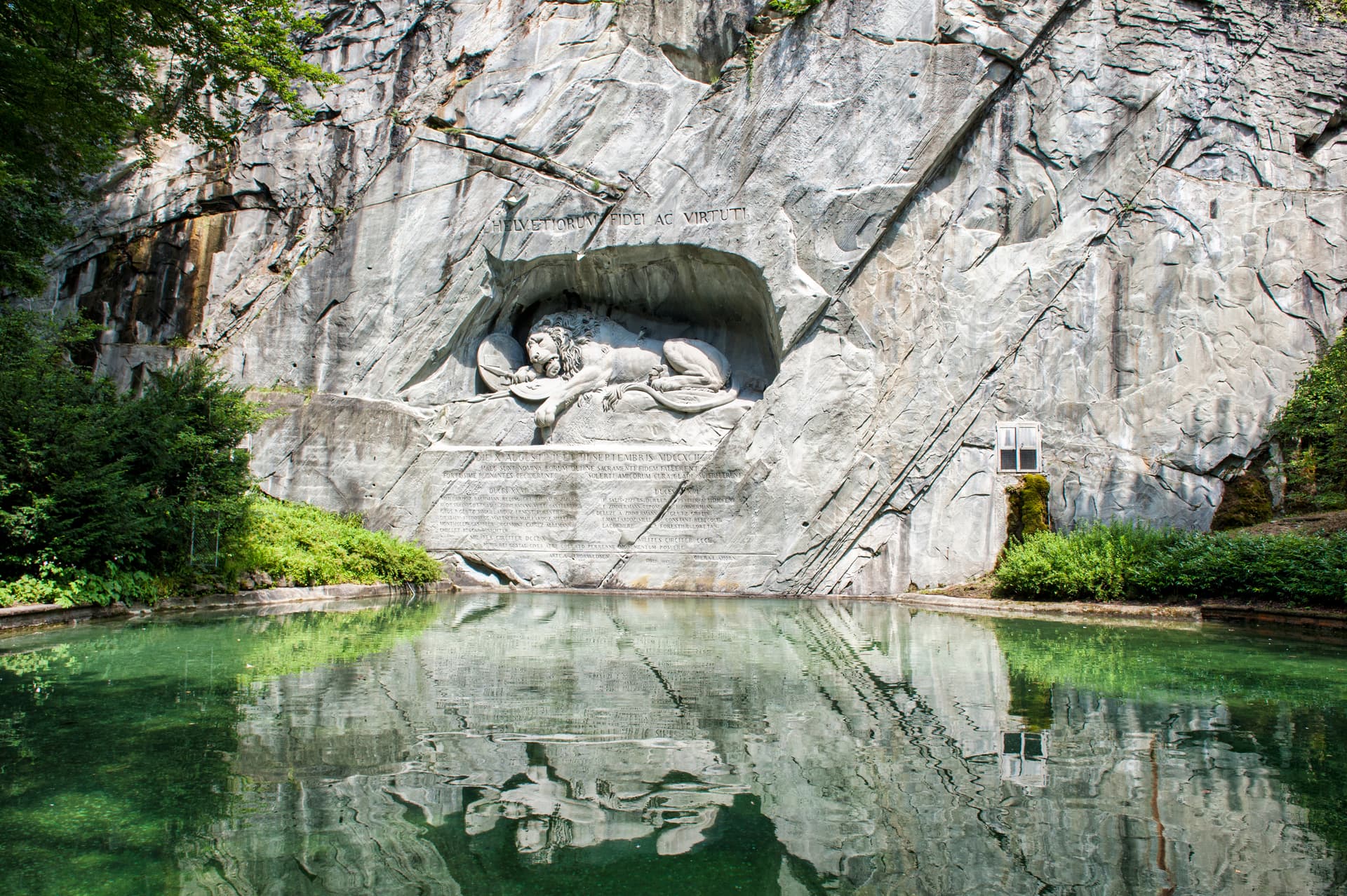 Lion Monument carved in rock face reflected in green pool in Lucerne, Switzerland.