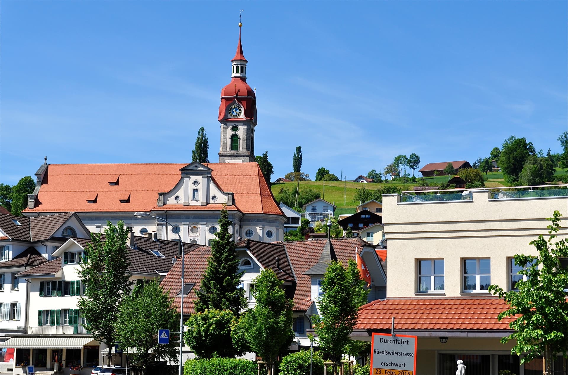 Church with red spire in Ruswil, Lucerne, Switzerland, under a clear blue sky.