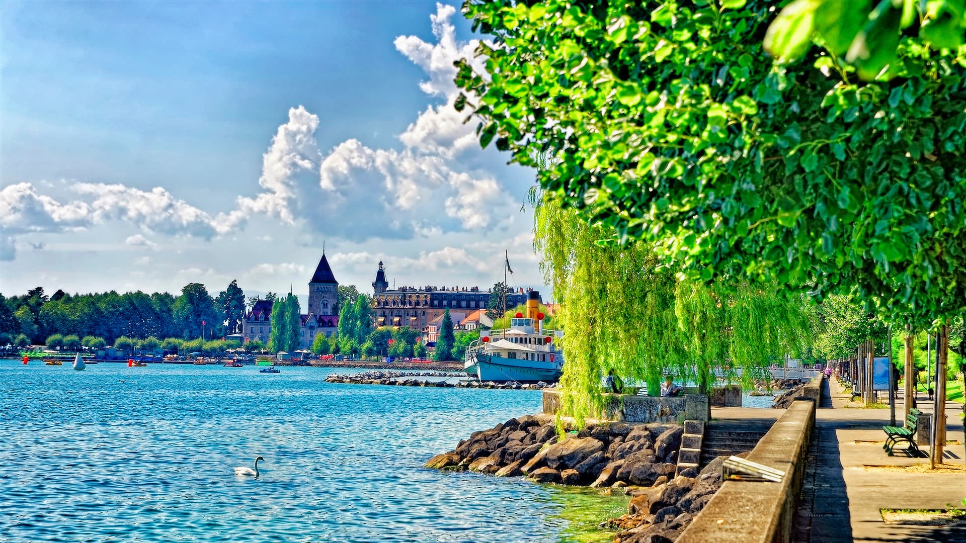 Castle of Ouchy near Lake Geneva with swan on water and lush green trees.