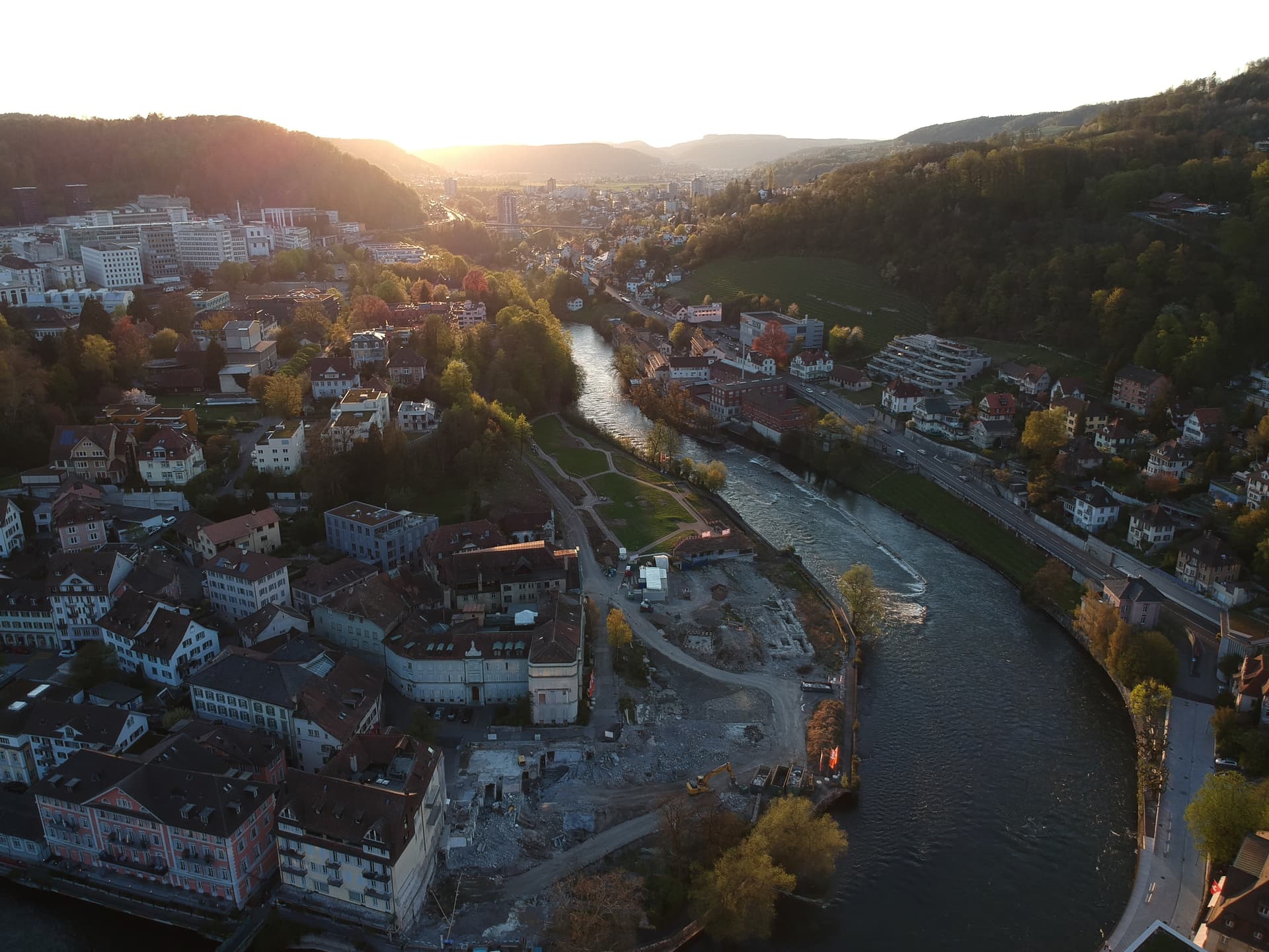 Aerial view of the Limmat river flowing through Baden with buildings nestled in sunlit hillsides.