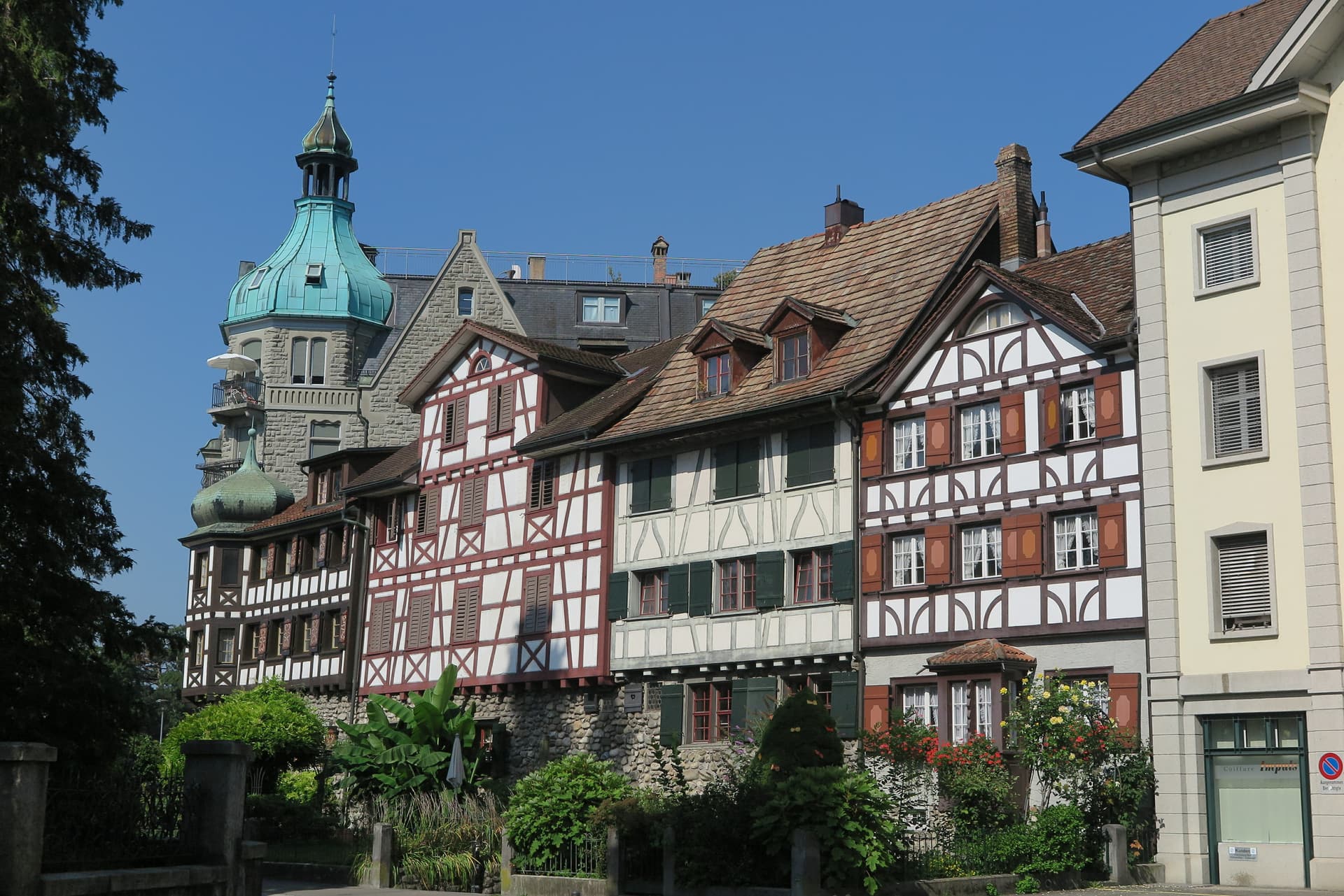 Half-timbered buildings and a stone structure with a green turret under a clear blue sky in Arbon am Bodensee.