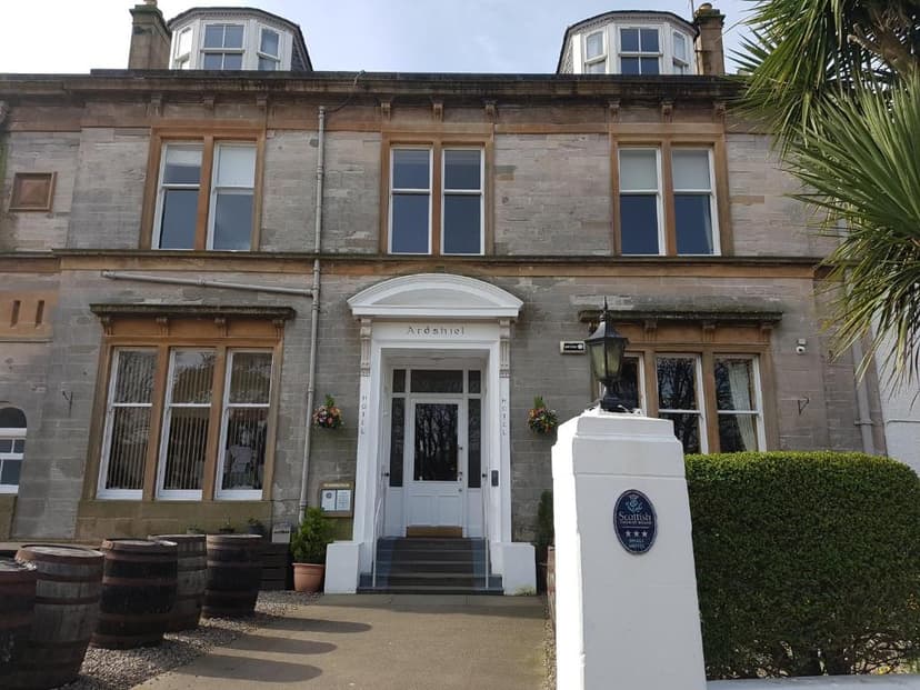 Ardshiel Hotel exterior with stone facade, white entrance, and whiskey barrels outside.