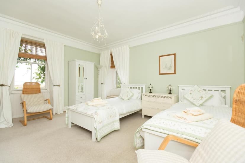 Twin bedroom with white furniture, pale green walls, and wicker chair near window