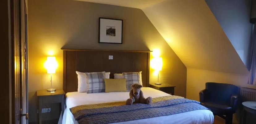Cozy hotel room with sloped ceiling, double bed, bedside lamps, and a teddy bear.
