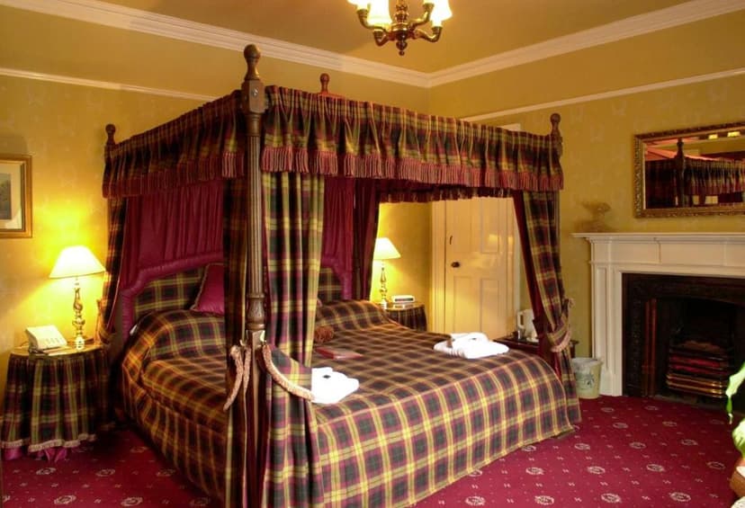 Four-poster bed with tartan bedding in a warmly lit hotel room at Atholl Arms.