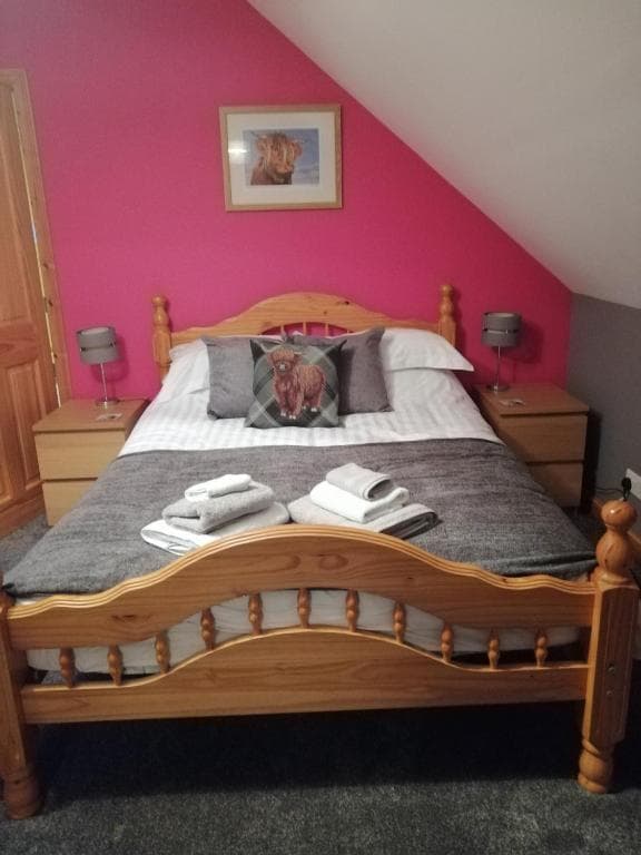 Double bed with wooden frame, pink wall, and Highland cow art in attic room