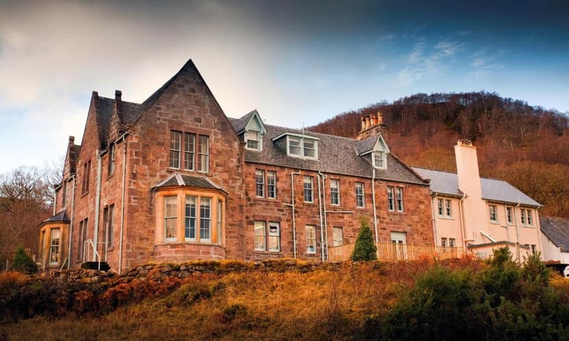 Loch Maree Hotel building with stone facade against a wooded hillside under a dramatic sky.