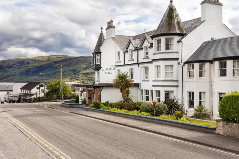 Caledonian Hotel building exterior with green mountains under cloudy sky