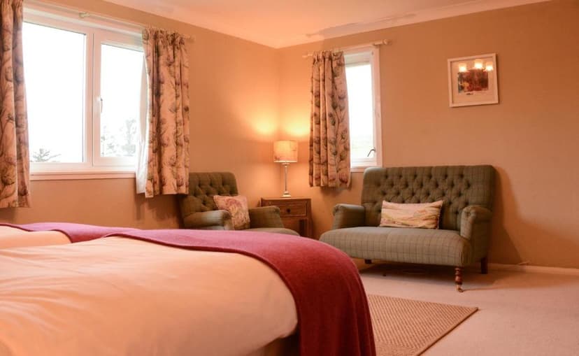Cozy hotel room with twin beds, green upholstered seating, and windows with patterned curtains in Scourie.