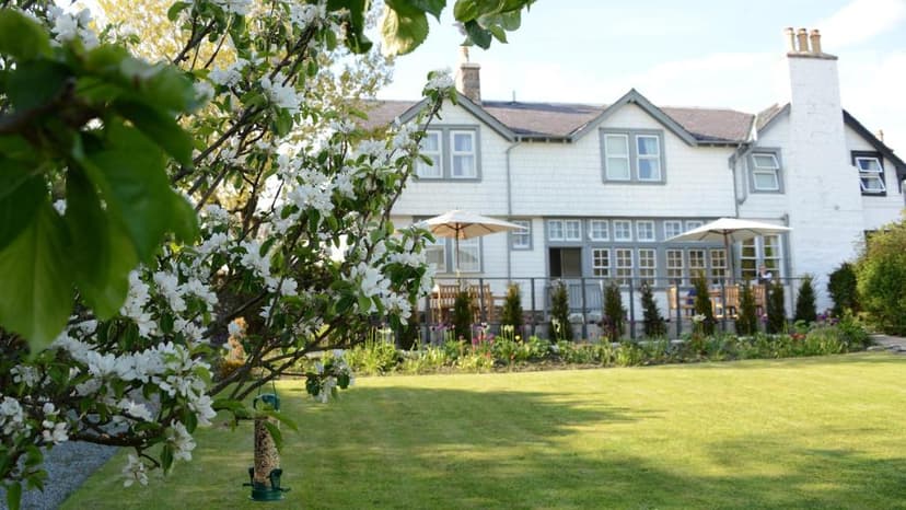 White hotel building seen over a blooming spring tree and green lawn at Scourie Hotel.
