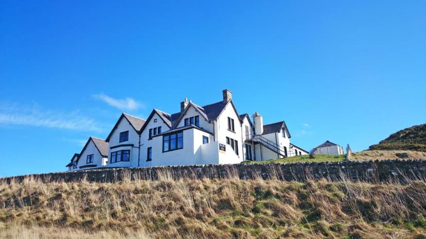 White hotel building perched on a grassy hill above a stone wall under a bright blue sky.