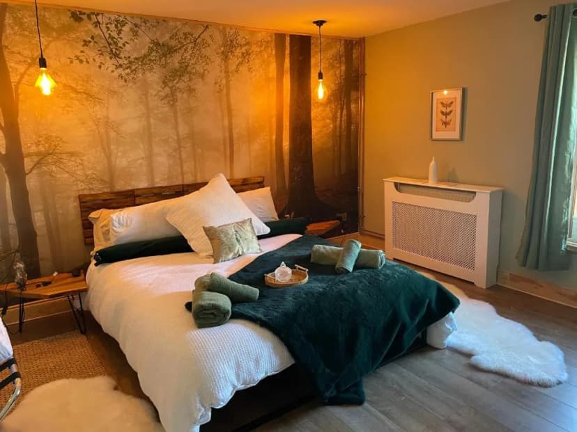 Cozy bedroom with forest mural, white bedding, green accents, and warm lighting