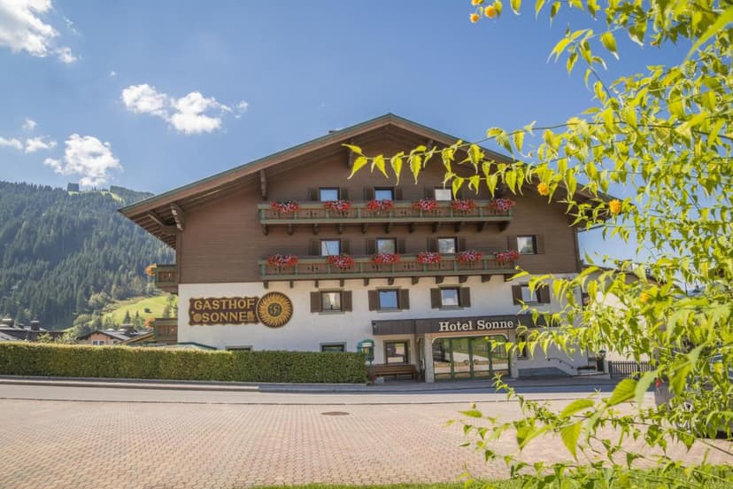 Gasthof Hotel Sonne building with flower boxes against a backdrop of forested mountains.