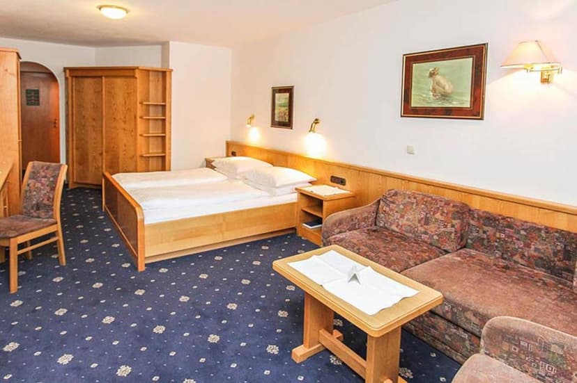 Hotel room with wooden furniture, twin beds, patterned sofa, and blue patterned carpet