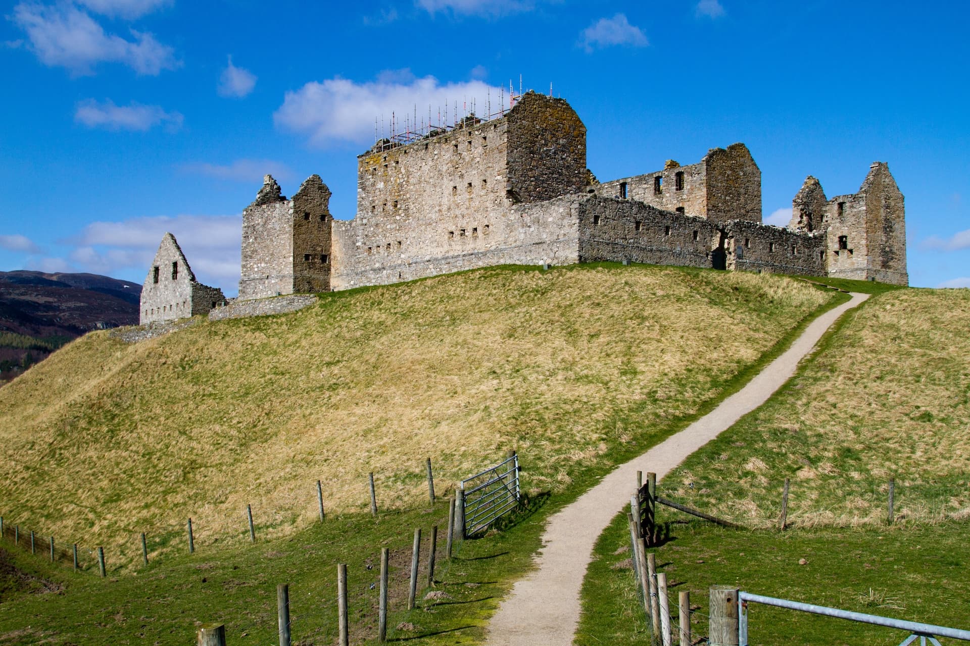 Ruined stone castle atop a grassy hill with scaffolding under a bright blue sky at Ruthven Barracks.