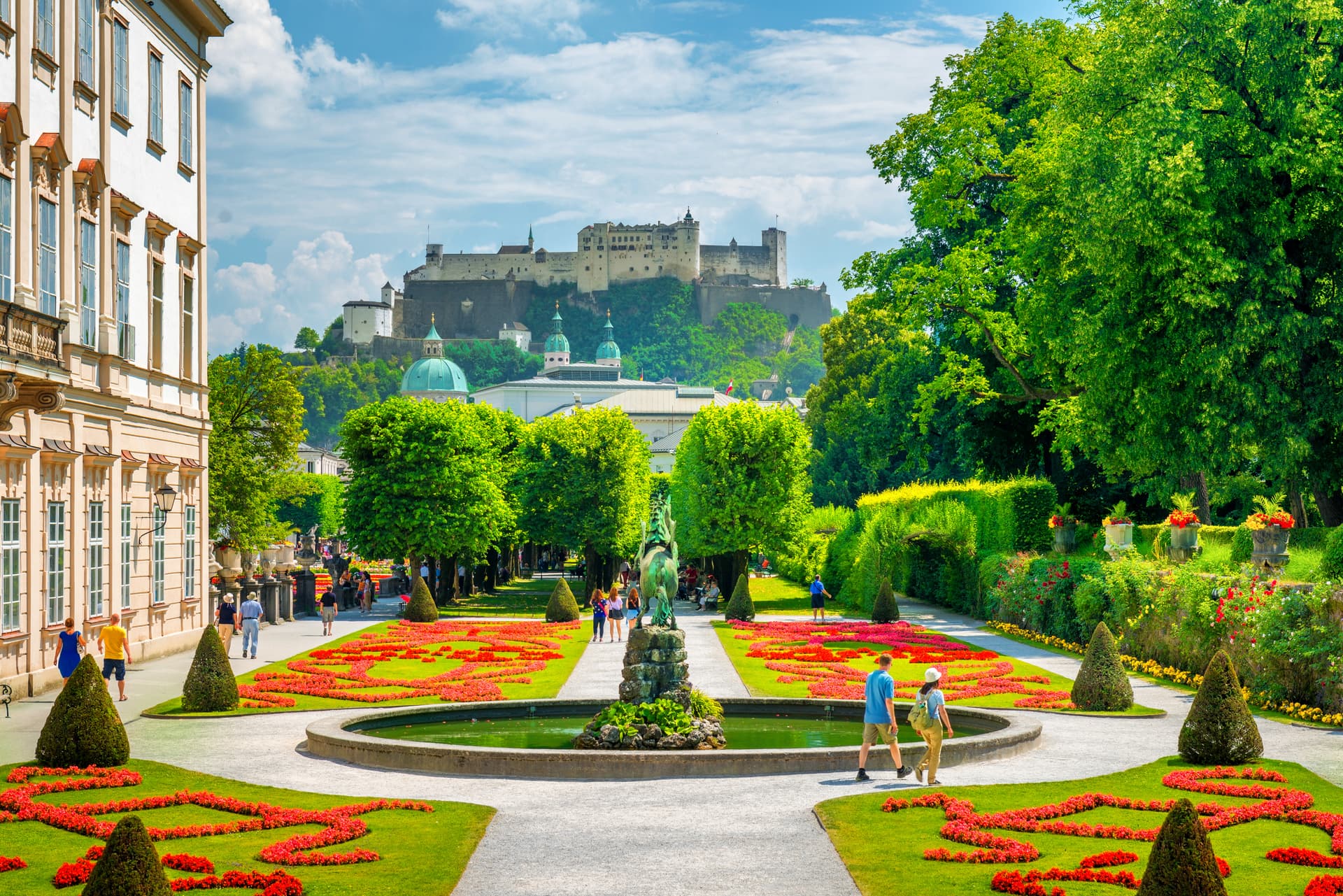 Formal gardens with red flowers, fountain, and Hohensalzburg Fortress in Salzburg.