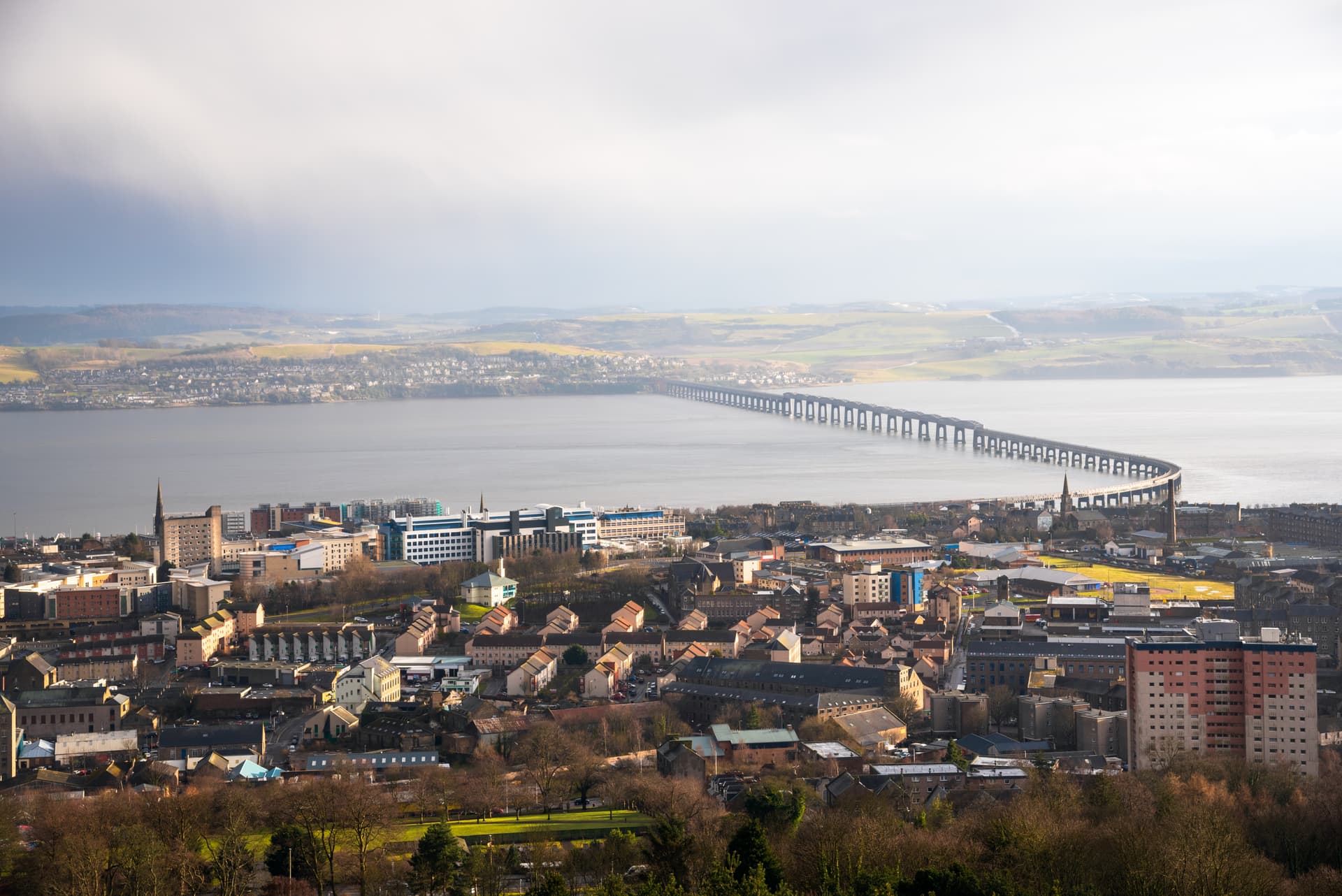 Panoramic view of Dundee city with the Tay Rail Bridge spanning the water under a bright sky.