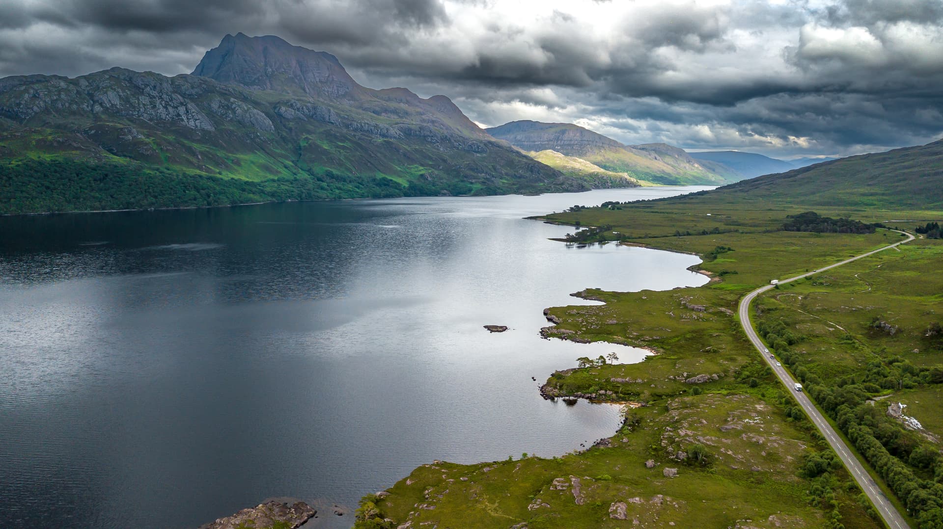 Loch Maree near Talladale with mountains under dramatic cloudy sky and road alongside water.