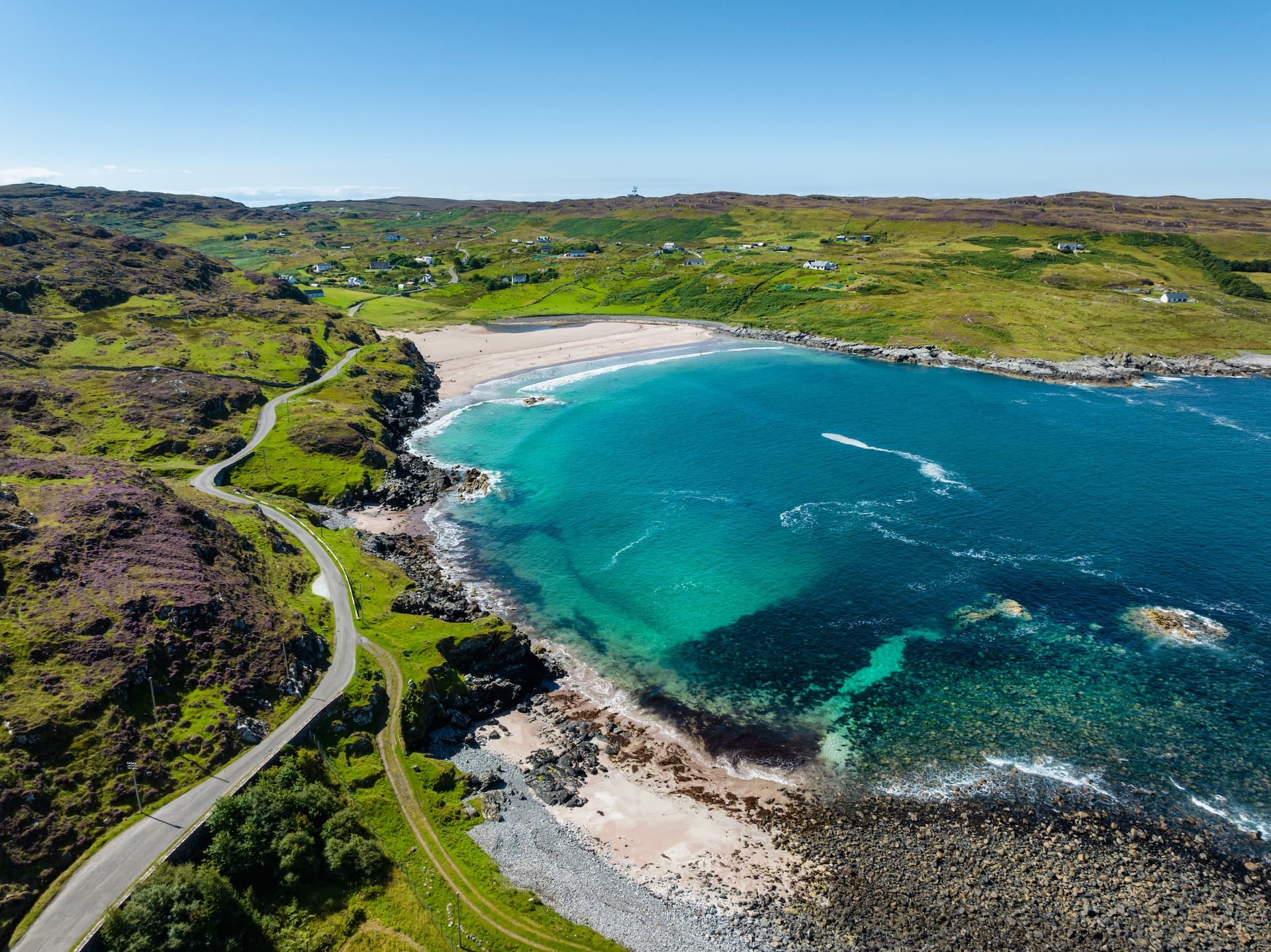 Aerial view of Clashnessie Bay with turquoise water, sandy beach, and winding coastal road.