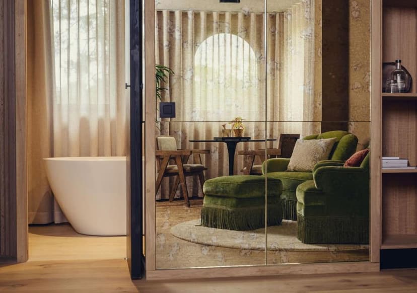 Modern hotel room with freestanding bathtub and green velvet seating reflected in mirrored wall.