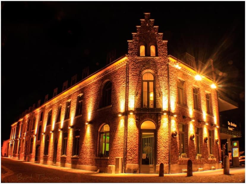 Brick building with stepped gable illuminated at night with warm uplighting in a European town.